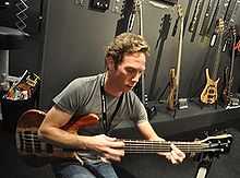 Young man playing bass in front of a display of other guitars