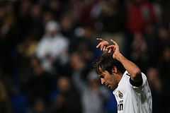 A long-haired man, wearing a white football shirt, with both hands lifted above his head