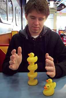 Randall Munroe balancing a stack of rubber duckies on a diner table.