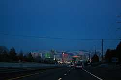 Dusk view of a freeway descending into a neon lit cityscape.