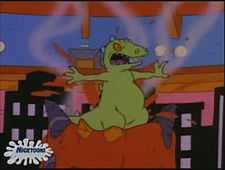 A cartoon large, green dinosaur angrily smashes through a fake volcano in an ice show.