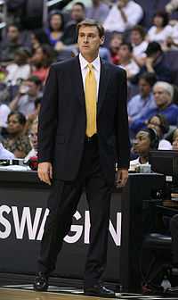 A man wearing a black suit is standing on the side of basketball court.