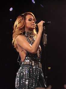 A dark blonde woman wearing a grayish shining outfit is performing