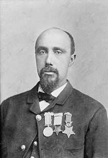 Head and shoulders of a balding black man with a goatee, wearing a suit coat, vest, and bow tie. On the jacket's left breast is a row of three medals.