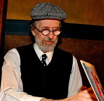 Photo of a bearded and bespectacled man opening a book