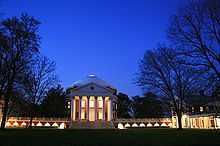 A red brick, Neoclassical dome with a large portico on the front and covered walkway on the sides lit up at dusk. Dark trees border the building on both sides.