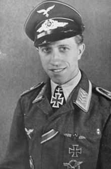 The head and upper body of a young man, shown in semi-profile. He wears a peaked cap and military uniform with various military decorations, at his neck, an Iron Cross displayed at the front of his white shirt collar.