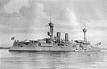 A large gray warship with two tall masts and two thin smoke stacks sits motionless offshore