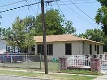 A color photograph of a small house with a fence in the front yard.