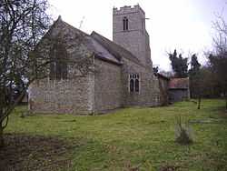 A flint church seen from the northeast showing the chancel, nave and aisle with a catslide roof, porch and battlemented tower