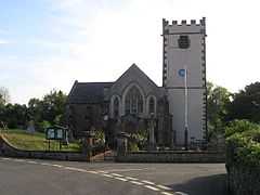 Stone building with white painted square tower. In the foreground is a road junction.