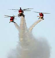 Three helicopters flying in formation, making smoke trails in the sky