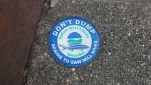 A blue and green circular medallion on a sewer warning that the discharge goes into the river