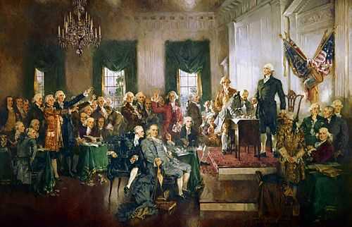A crowd of men gathered in a hall with chandeliers and American flags.