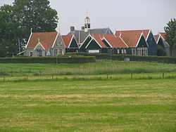 About 10 small buildings of dark wood with steeply peaked red roofs. In the center is a larger building with a grey roof and a small clock tower.