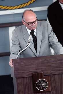 Late-twentieth-century man in a suit standing at a podium.