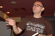 A man with the shot focused on his upper body. He is wearing a pair of glasses and a brown shirt.