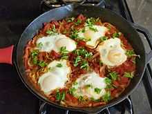 Five cooked eggs on top of tomato sauce in cast iron skillet