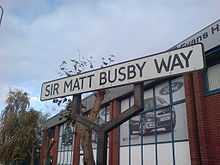 A white road sign with a black border and the words "Sir Matt Busby Way" in black capital letters.
