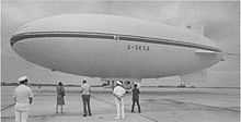 An airship standing on an airfield with several people looking at it