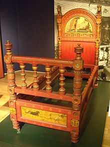 Photograph of a bed showing paintings on the headboard and the foot of the bedframe