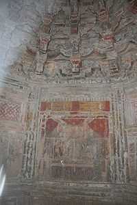 A small interior stone room with paintings that still retain some yellow and red coloring. Above the painting are at least three levels of stone support brackets.