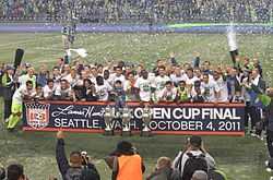 Several players are standing together with three trophies on the ground in front of them