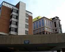 Two towers, one dark red brick, one half brick and half stone rise over a multi-story parking garage.