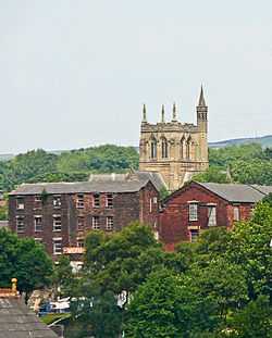 A church tower with pinnacles and a tall stair turret rising above brick buildings in the foreground