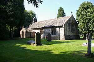 A low small stone church with a south porch and west bellcote.
