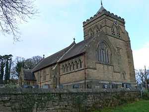 A large broad church seen from the northwest showing a large chancel, the nave, a porch and a broad castellated tower beyond the chancel; a wall in the foreground