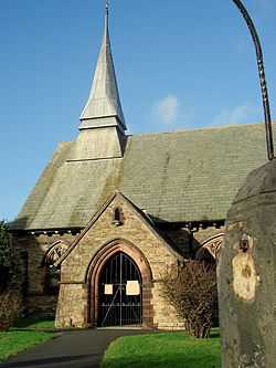 The west end of the church showing the porch and small tower; part of a gatepost intrudes on the right