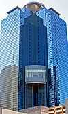 Ground-level view of a blue, glass high-rise; a circular pad sits atop the structure