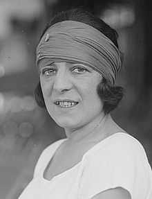 A woman looking at the camera with a colored bandanna on and a white shirt, which this picture is black and white