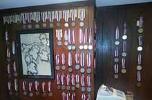 A wood-paneled room with many medals and a drawing of a grapevine hanging on the wall, and a cash register at the bottom.