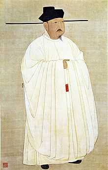 Painted image of a man standing erect, wearing white silk robes, black hat, black shoes, and sporting a black mustache and goatee