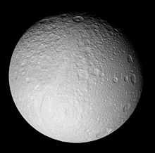 A spherical heavily cratered body is illuminated from the bottom. The terminator runs from the left to right in the vicinity of the top limb. There is a wide curved graben running from the center of the body to the bottom. It is Ithaca Chasma.