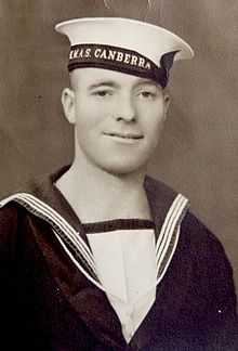 A black-and-white photograph of a man looking at the viewer and wearing a uniform and a hat reading "HMAS CANBERRA" around the brim