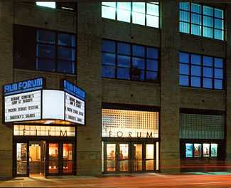 The front of a movie theater, with bright lights at the entrance and a blue backdrop on the second and third floors. The marquee is advertising a film by Ousmane Sembène and the original "Solaris" from 1972.
