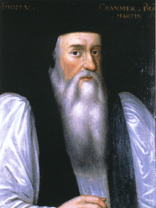 Portrait of Archbishop Cranmer as an elderly man. He has a long face with a flowing white beard, large nose, dark eyes and rosy cheeks. He wears clerical robes with a black mantle over full white sleeves and has a doctoral cap on his head