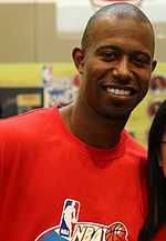 Headshot of a young black man wearing a red t-shirt. He is smiling.