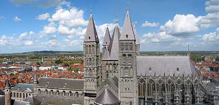 A grey stone cathedral with a central square tower flanked by 4 square towers. Surrounded by the red roofs of the old city.