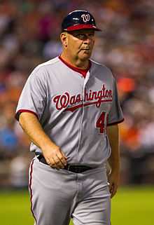 A photograph of a man wearing a gray baseball jersey and pants with "Washington" written across the chest in script and a batting helmet with a "W" on it.