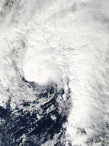 Satellite image of a comma-shaped tropical cyclone just off the United States Gulf Coast. All land in the image is obscured by cloud cover which extends in all directions, except southwest, from the center of the storm.