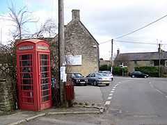 Street scene. Red telephone box and telegraph pole. Stone buildings around road junction.