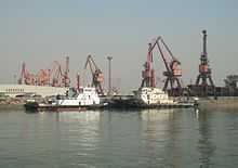 two black and white tugboats berthed against a background of large cranes