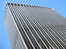 Street view of top half of skyscraper against the sky; its outside is dominated by vertical black and white lines