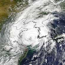 Satellite image of a loosely defined, but spiral-form cluster of clouds nearing a landmass.