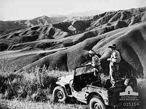 Soldiers in a stationary jeep view steep undulating countryside