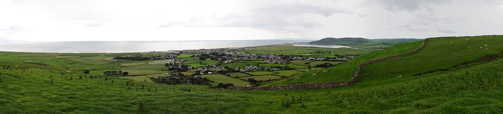 Panorama of the Welsh town Tywyn showing it nestled between hills and with the sea behind. A reservoir is visible in the background.